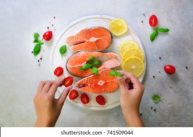 Women's Hands Are Preparing Salmon Steaks On Grey Concrete Background. Top View. Preparation Ingredients For Cooking Fish Food. Copy Space