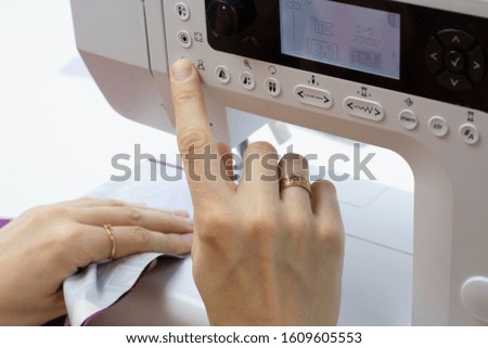 Women's hands sew clothes on a sewing machine. Close-up photo, white background.