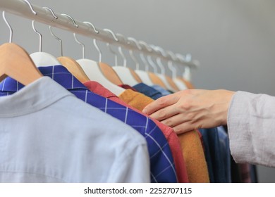 women's hands sort through clothes in wardrobe on hangers, shopping and selection of look for work and meetings. female stylist helps to buy clothes. recycling of textiles, cluttering of the closet at