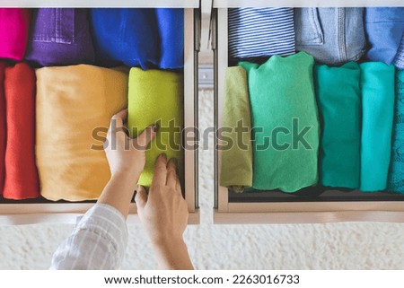 Women's hands take bright rainbow clothes from a wardrobe drawer. The concept of order and storage. Vertical storage method. Topview.