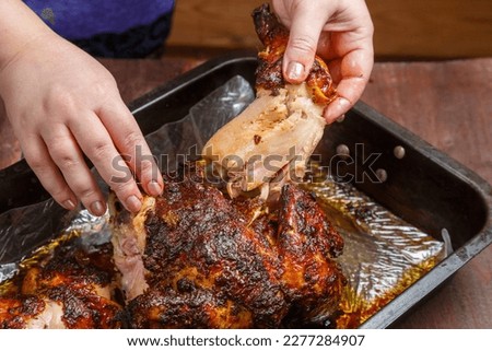 Women's hands tear off a ham from a whole baked chicken in a baking sheet..Horizontal photo.
