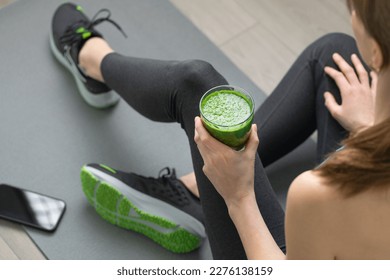 Women's hands tying sport shoes on a gray workout mat. With smoothie for detox in background. Healthy living, dieting lifestyle. - Shutterstock ID 2276138159