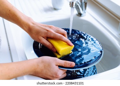 Women's hands wash dirty plate with sponge for dishes under stream of water from tap. concept of cleaning dirty dishes after eating, household chores, kitchen sink, water consumption - Shutterstock ID 2208431101