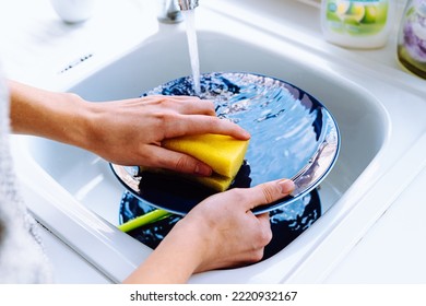 Women's hands wash dirty plate with sponge for dishes under stream of water from tap. concept of cleaning dirty dishes after eating, household chores, kitchen sink, water consumption - Shutterstock ID 2220932167