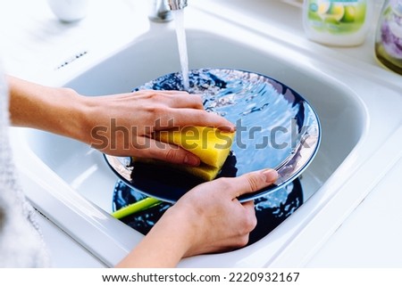 Women's hands wash dirty plate with sponge for dishes under stream of water from tap. concept of cleaning dirty dishes after eating, household chores, kitchen sink, water consumption