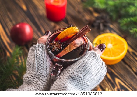 Women's hands in a white warm sweater are holding a glass cup with mulled wine. Concept of a cozy atmosphere and a nice winter mood with a aromatic hot traditional drink.