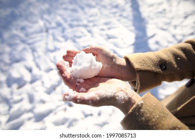 Women's hands in winter without gloves make a snowball and make a heart out of it