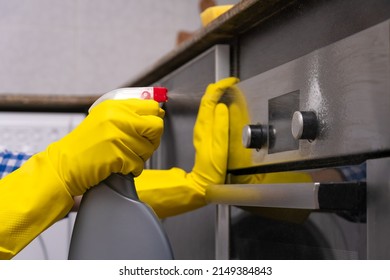 Women's hands in yellow rubber gloves are rubbing cleaning agent on the surface of the oven in the home kitchen. Concept of housework and housekeeping