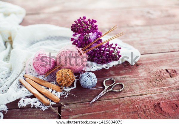  Women\'s hobby. Crochet and knitting.\
Working space. Pink balls of yarn, needles, scissors, crochet hooks\
on the wood table  in the cozy home.\
\
