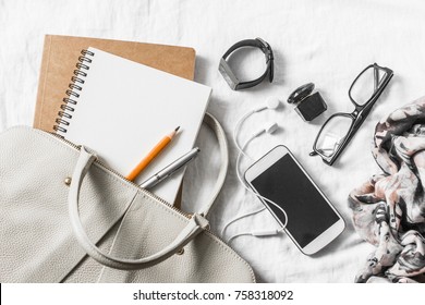 Womens Leather Handbag, Clean Blank Notepad, Pen, Glasses, Smartphone, Earphone, Watch, Perfume, Scarf On A Light Background, Top View. Free Space For Text. Woman Workplace Business Background