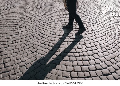 Women's Legs In Black Jeans And Winter Boots Walk Along Gray Granite Paving Stones And Casts A Contrasting Shadow.. The Concept Of A Walk In The Old City.