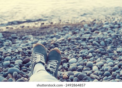 Women's legs in green sneakers on a pebble beach by the sea at sunset. Image of rest and relaxation - Powered by Shutterstock