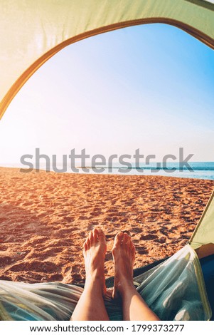 Women's legs out of the tent. Vacation camping on the sea beach
