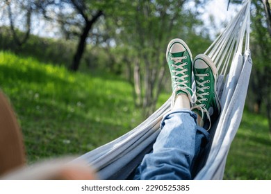 Women's legs shod in green sneakers on a hammock in a summer garden. Summer holidays vacation concept - Powered by Shutterstock