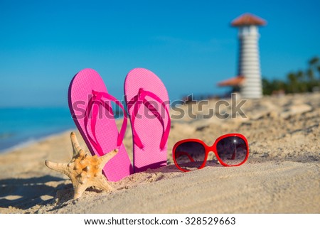 Women's marine accessories: sandals, sunglasses and starfish on tropical sand beach against the background of  lighthouse