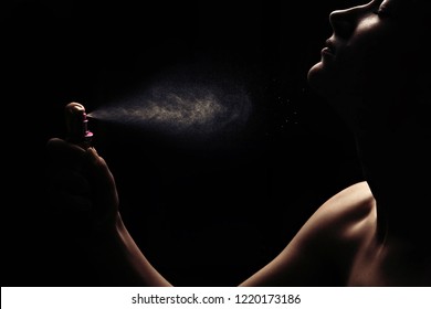 Women's perfume spraying on black background. Girl use perfume with amazing fragrance. Silhouette of sexy girl body with perfume.