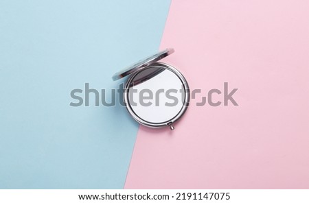 Women's portable make-up mirror on a blue-pink pastel background. Top view
