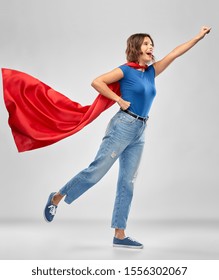 Women's Power And People Concept - Happy Woman In Red Superhero Cape Making Flying Pose Over Grey Background