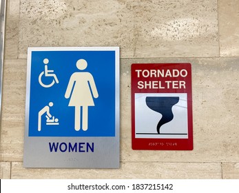 The Women's Restroom And Tornado Shelter Signs Directing People To The Shelter In A Public Building.