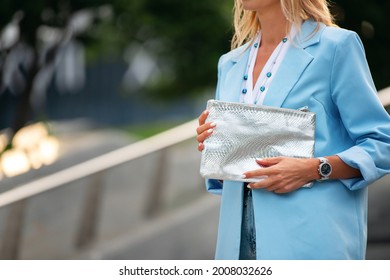 Women's silver clutch bag with snakeskin texture. Fragment of the body of a model in a summer blue jacket, white blouse. Business attire and beads. - Shutterstock ID 2008032626
