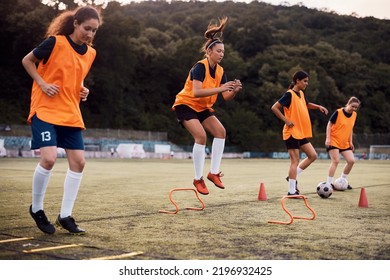 Women's soccer team practicing on playing field. Focus is on player jumping over obstacles.   - Powered by Shutterstock