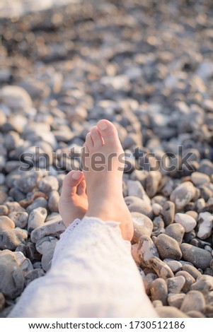 Women's toes on a stone beach during sunset with white dress 