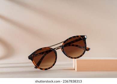 Womens Tortoiseshell frame sunglasses on a podium on beige background with shadows. Trendy sunglasses still life in minimal style. Summer fashionable accessories. Optic store discount, sale - Shutterstock ID 2367838313