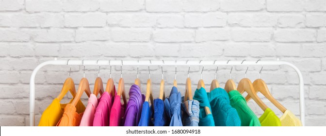 Women's wardrobe sweatshirts shirts and blouses hang on wooden shoulders in the order of all the colors of the rainbow against white brick wall. Concept update in the wardrobe. Advertising space - Powered by Shutterstock