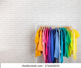 Women's wardrobe sweatshirts shirts and blouses hang on wooden shoulders in the order of all the colors of the rainbow against white brick wall. Concept update in the wardrobe. Advertising space - Powered by Shutterstock