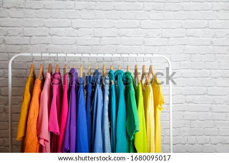 Women's wardrobe sweatshirts shirts and blouses hang on wooden shoulders in the order of all the colors of the rainbow against white brick wall. Concept update in the wardrobe. Advertising space