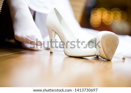 Women's white high heels on the wooden floor next to the female foot in stockings