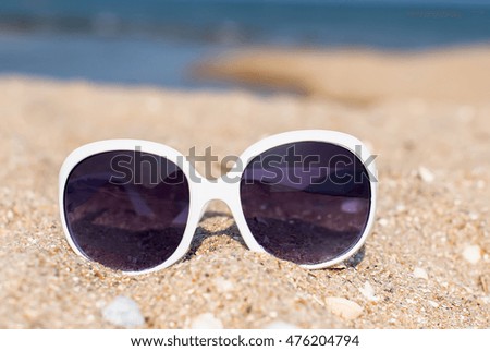 Women's white sunglasses in the sand overlooking the sea, the concept of summer beach holidays