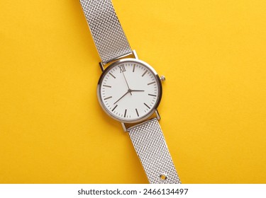 Women's wrist analog watch with metal or silver strap on yellow background - Powered by Shutterstock
