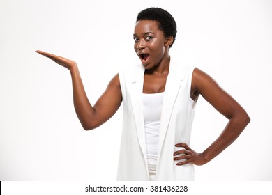 Wondered excited african american young woman standing and holding copyspce on palm over white background