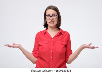 Wondered Woman In Glasses And Red Shirt Isolated On White Wall. I Do Not Know What To Choose. Studio Shot