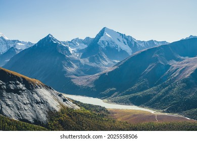 Wonderful alpine landscape with mountain lake and mountain river in valley with forest in autumn colors on background of snowy mountains silhouettes under blue sky. Beautiful mountain valley in autumn - Shutterstock ID 2025558506