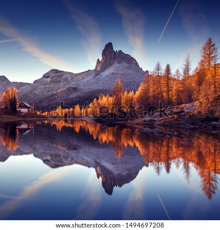 Wonderful autumn landscape during sunset. Fairy tale moutain lake with picturesque sky, majestic rocky mount and colorful trees glowing sunlight. Amazing nature scenery. Federa lake. Dolomites Alps.