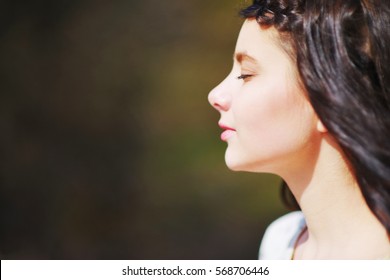 Wonderful Beautiful Dreamy Woman Meditating Outdoors With Eyes Closed, With A Blur Effect On A Dark Green Background Closeup. Face Meditation