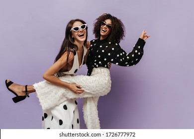 Wonderful black girl in black blouse and trendy white pants laughing and having fun with her friend in sunglasses on isolated backdrop. - Powered by Shutterstock