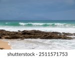 Wonderful blue sea with its rocks emerging from the sand at Langs Beach. January 20, 2024, New Zealand, Northland, Whangarei, Bream Bay, Langs Beach.