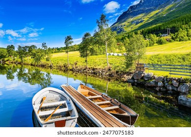 Wonderful boats moored on the pier. Shallow lake Eidsvatnet in the mountains of Norway. Summer in Scandinavia. The water reflects lush clouds, blue skies and forested shores.  - Powered by Shutterstock