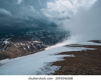 Wonderful dramatic landscape with big snowy mountain peaks above low clouds. Snow storm on top of a mountain. Atmospheric large snow mountain tops in cloudy sky.
