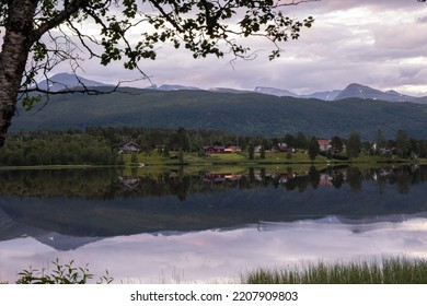 Wonderful landscapes in Norway. Nordland. Beautiful scenery of a valley with houses on the hill. Mirror in the lake. Calm water in a cloudy summer day. Snowed mountains in background. Selective focus