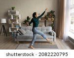Wonderful life. Overjoyed happy millennial hispanic woman dance at modern living room in playful mood enjoy weekend leisure time. Carefree young lady having fun celebrate freedom after cleaning home