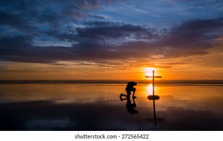 Wonderful Reflection On A Beach At Sunset, With A Man Kneeling By It.