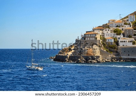 Wonderful seaview of Hydra island, cascade of the houses on the hill over the deep blue sea water. Port city landscape with a yacht o the dark blue water and red rooves of residential buildings.