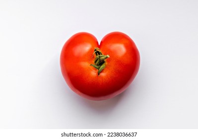 Wonky shaped red tomato in the shape of a heart shot from above on a white surface.
