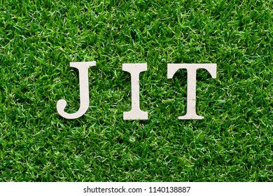 Wood alphabet in word JIT (abbreviation of just in time) on artificial green grass background