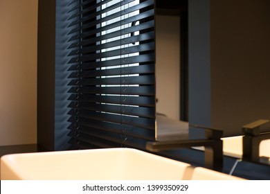 Wood blinds black color closeup on the window. Wooden slats 50mm wide. Venetian blinds in the bathroom. Black tapes, mirror near the washbasin.