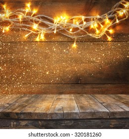 Wood Board Table In Front Of Christmas Warm Gold Garland Lights On Wooden Rustic Background. Filtered Image. Selective Focus. Glitter Overlay